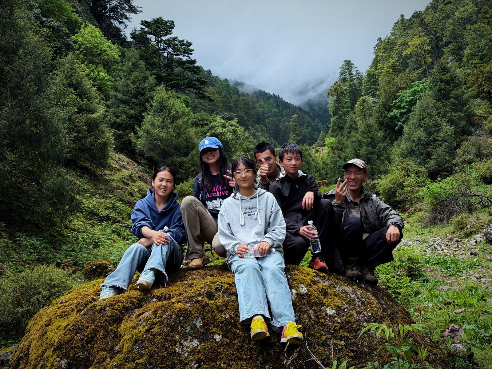 Volunteers sitting together on a moss-covered boulder in the forest above Liju